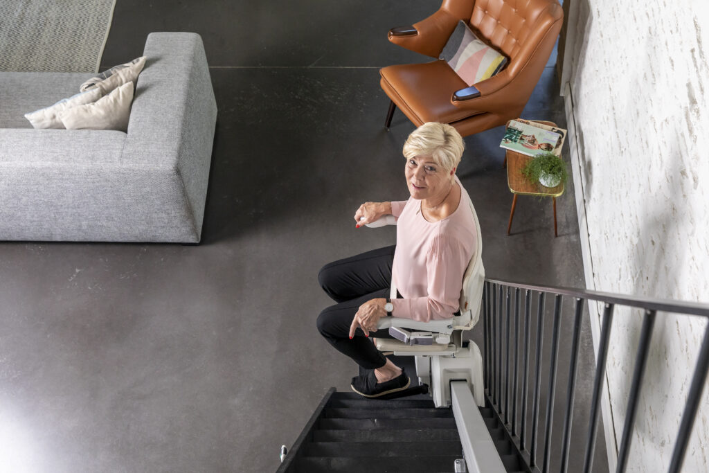 Mobility Scotland - Mobility Scotland Announce Fantastic New Stairlift Rental Service 1100 woman sitting stairlift downstairs Mobility Scotland - Mobility Scotland Announce Fantastic New Stairlift Rental Service 1100 woman sitting stairlift downstairs
